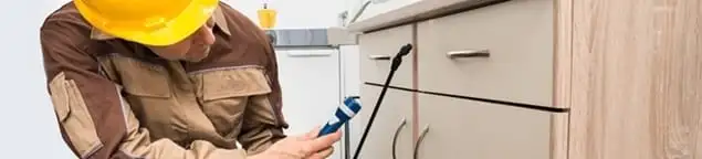 Roach exterminator applying treatment under kitchen cabinets in Toledo, OH