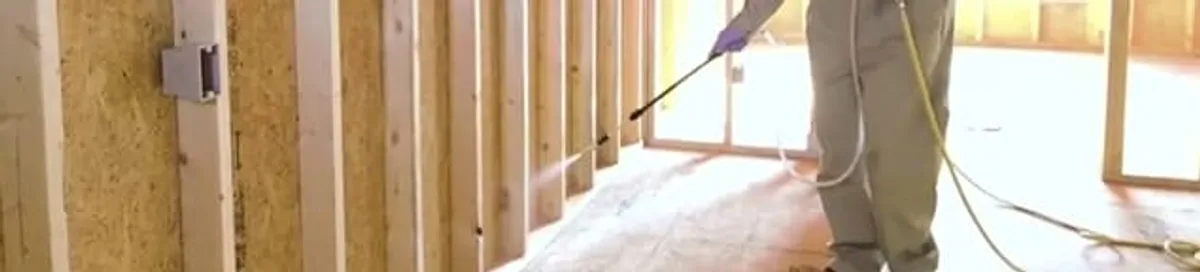 Termite treatment technician applying spray along framing and unfinished walls in Toledo, OH