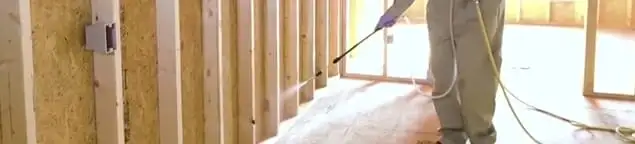 Termite treatment technician applying spray along framing and unfinished walls in Toledo, OH